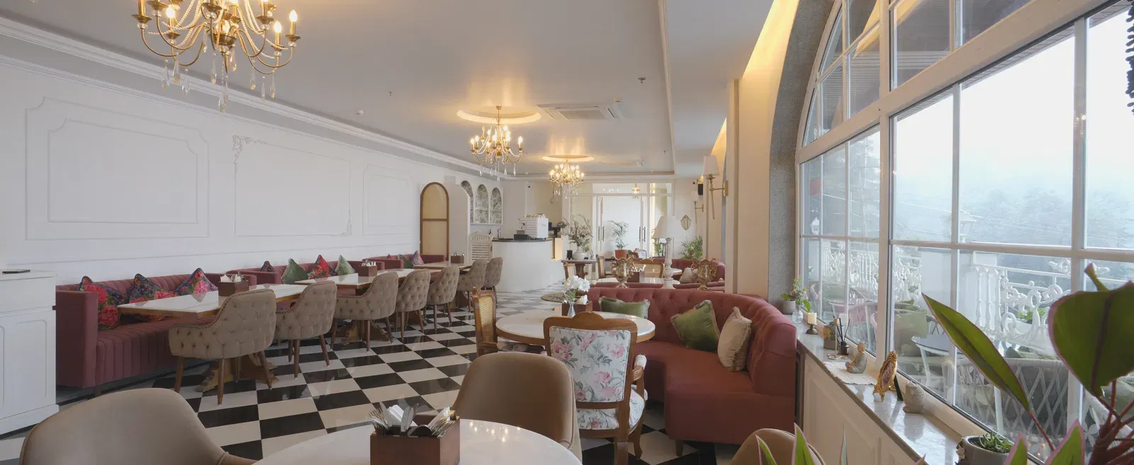 Sun-lit dining area with chandeliers, white tables, and cushioned booths - Mayfair Cafe & Suites, Dalhousie