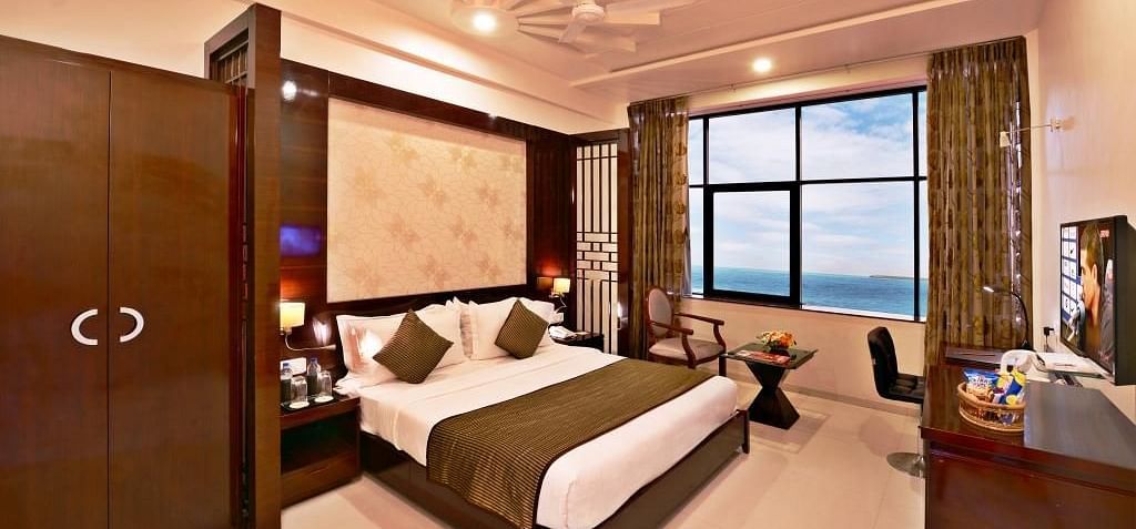A cosy hotel room includes a king size bed with patterned bedding, a seating area near a window with a view, and warm lighting.