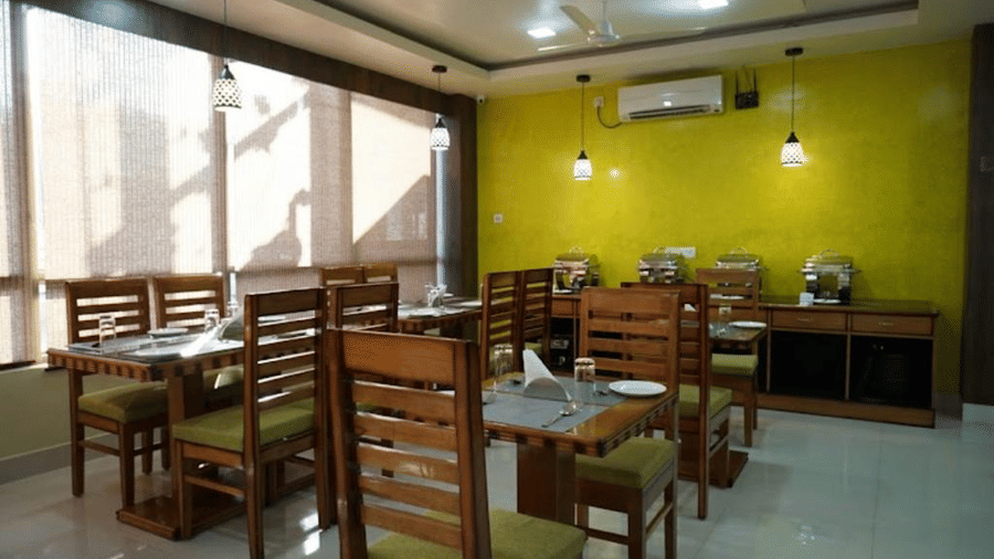A well-lit dining area with wooden furniture and vibrant green walls, perfect for relaxed meals at Pemaling Lords Eco Inn Guwahati