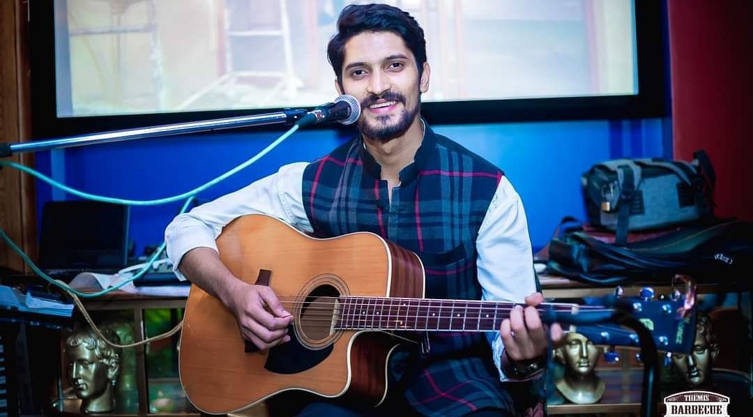 An image of a man playing guitar and singing on a mic at the same time at Themis Barbecue House, NSP Panipat