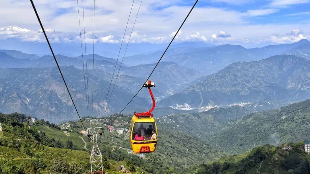 Ropeway cable cars gliding over lush green hills, offering panoramic mountain views.