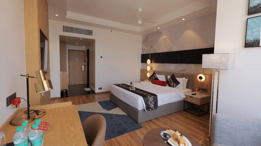 Comfortable guest room at Lords Inn Somnath featuring a king-size bed, seating area, work desk, television and modern wooden furnishings for a pleasant stay.