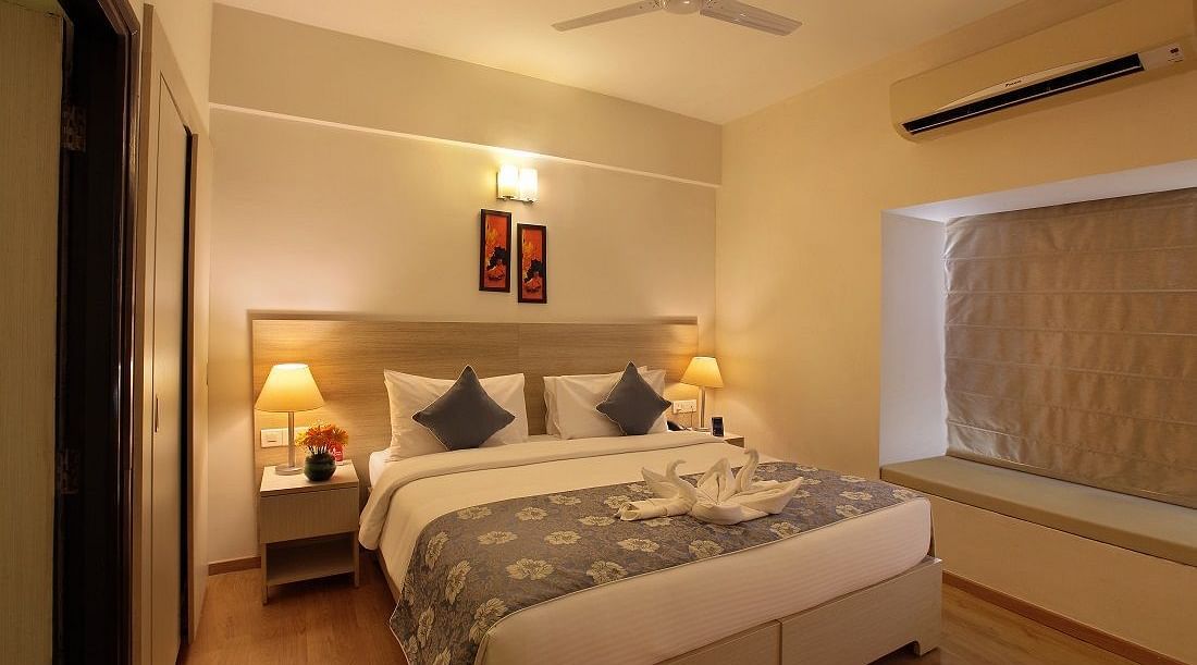 Premium room at Starlit Suites, Bangalore features a double bed with patterned bedding and cushions, bedside tables with lamps, and a window beside.