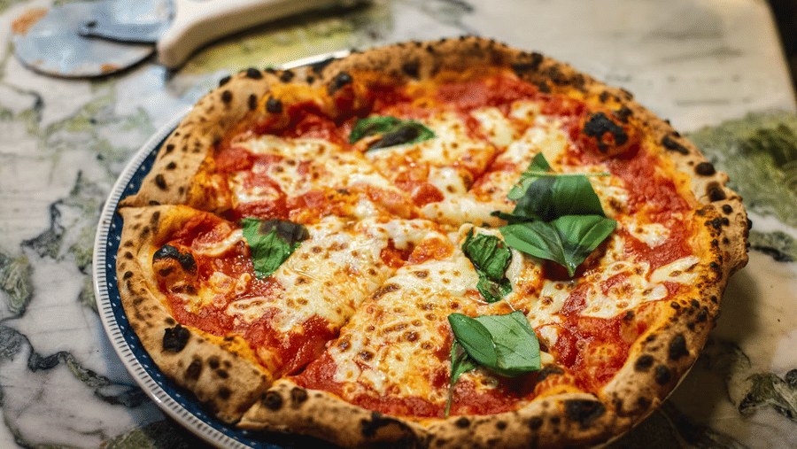 Margherita pizza with a charred crust, melted mozzarella, tomato sauce, and fresh basil leaves served on a plate on a marble table.