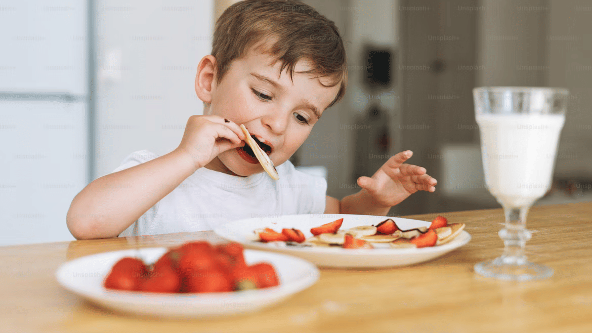 A toddler boy having milk, berries, and pancake