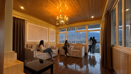 A spacious room interior with seating area, wooden flooring, large windows, and guests near the window at Avianna Group Of Hotels & Resorts.