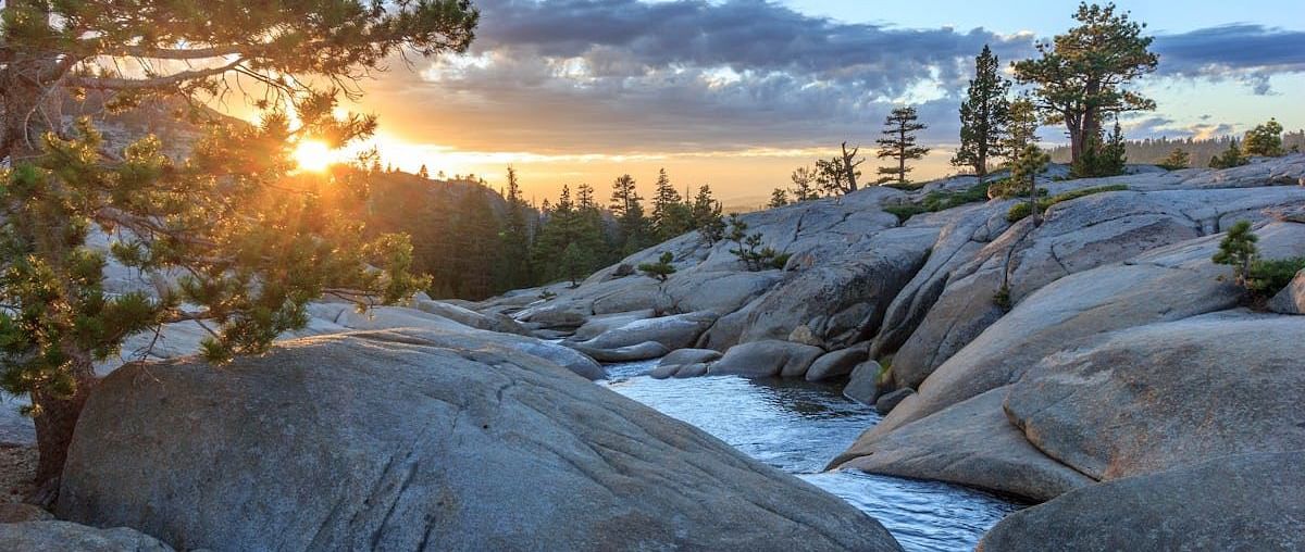 Sun setting behind the forest with large boulders in the foreground - Amador Hotel.