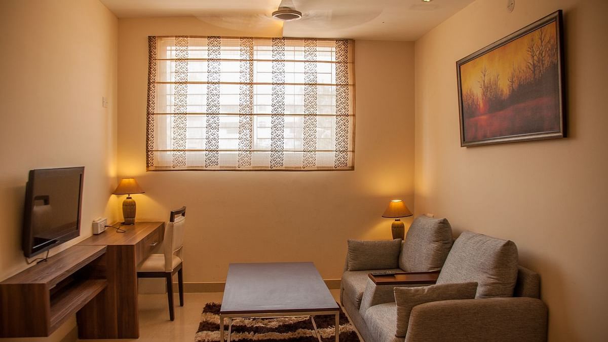 A living room with a sofa, table, television, and a window with blinds | Astra Hotels and Suites Electronic City