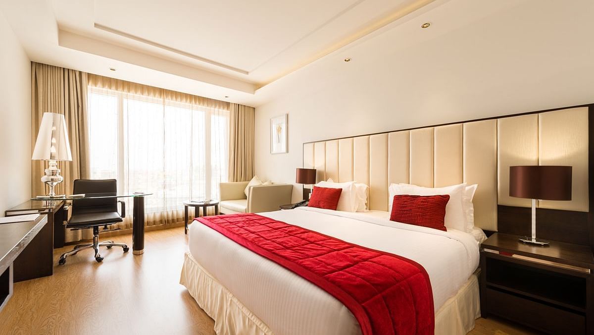 A well-lit hotel room with two twin beds covered in red bedspreads and white sheets - TGI Grand Fortuna, Hosur