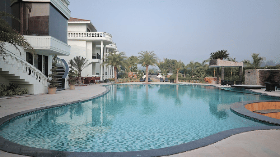 Large resort pool area flanked by modern white villas with balconies and tropical palm trees.