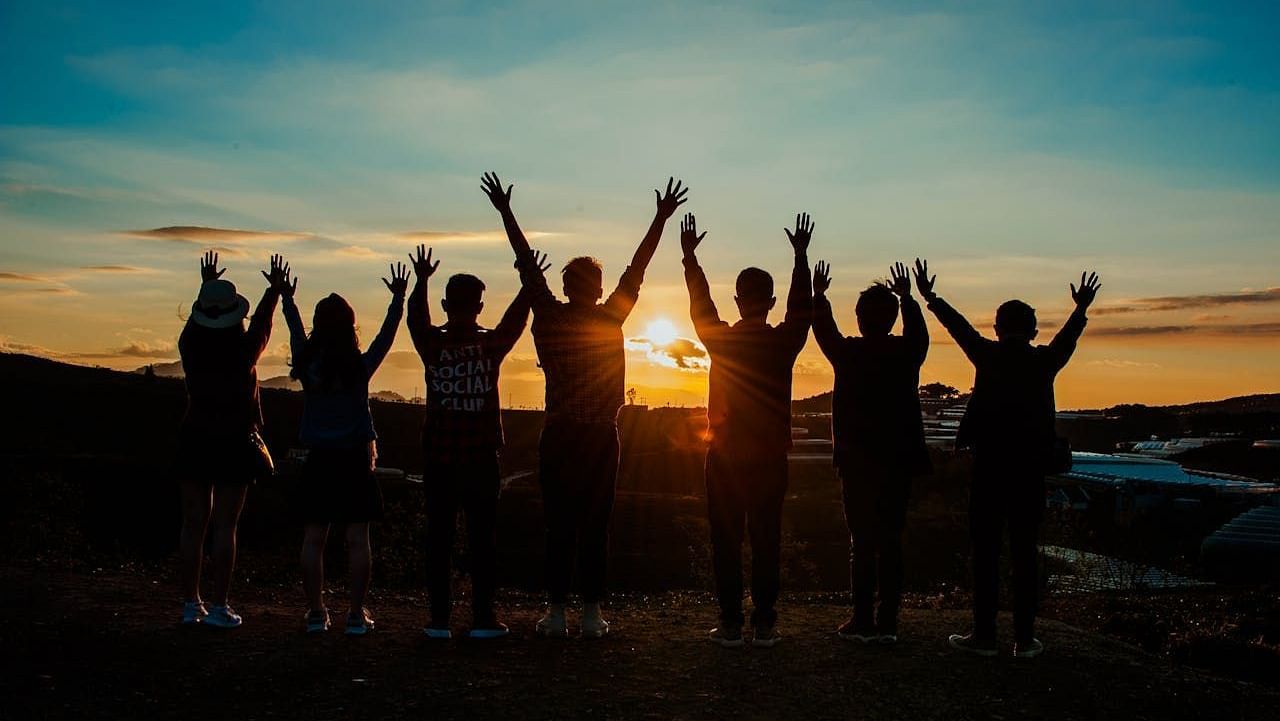 A silhouette of a group of people with raised hands, while watching the sun - Avianna Group of Hotels & Resorts