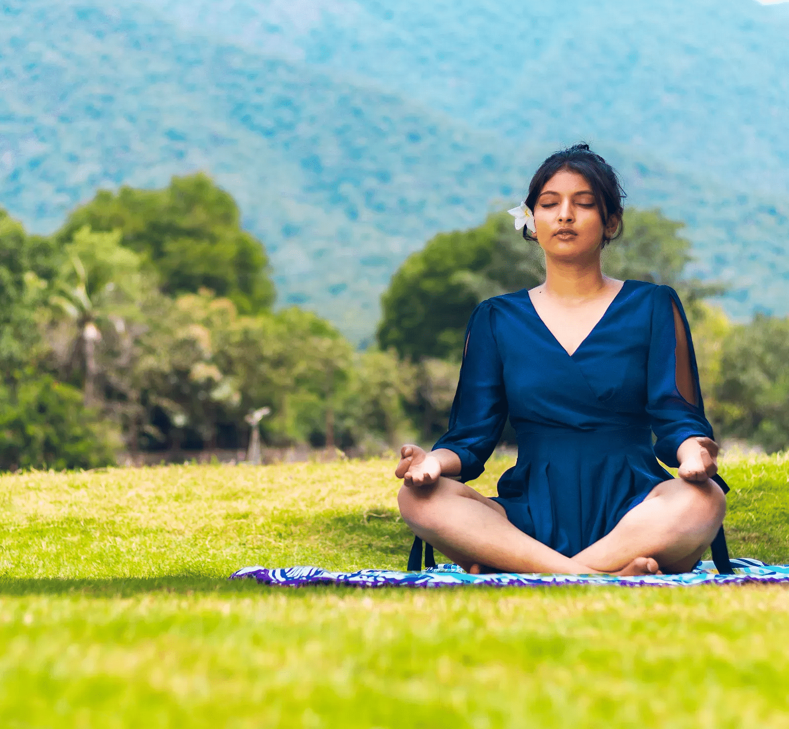 A lady sitting on a mat, doing meditation with a luscious greenery scene behind near Avana resort