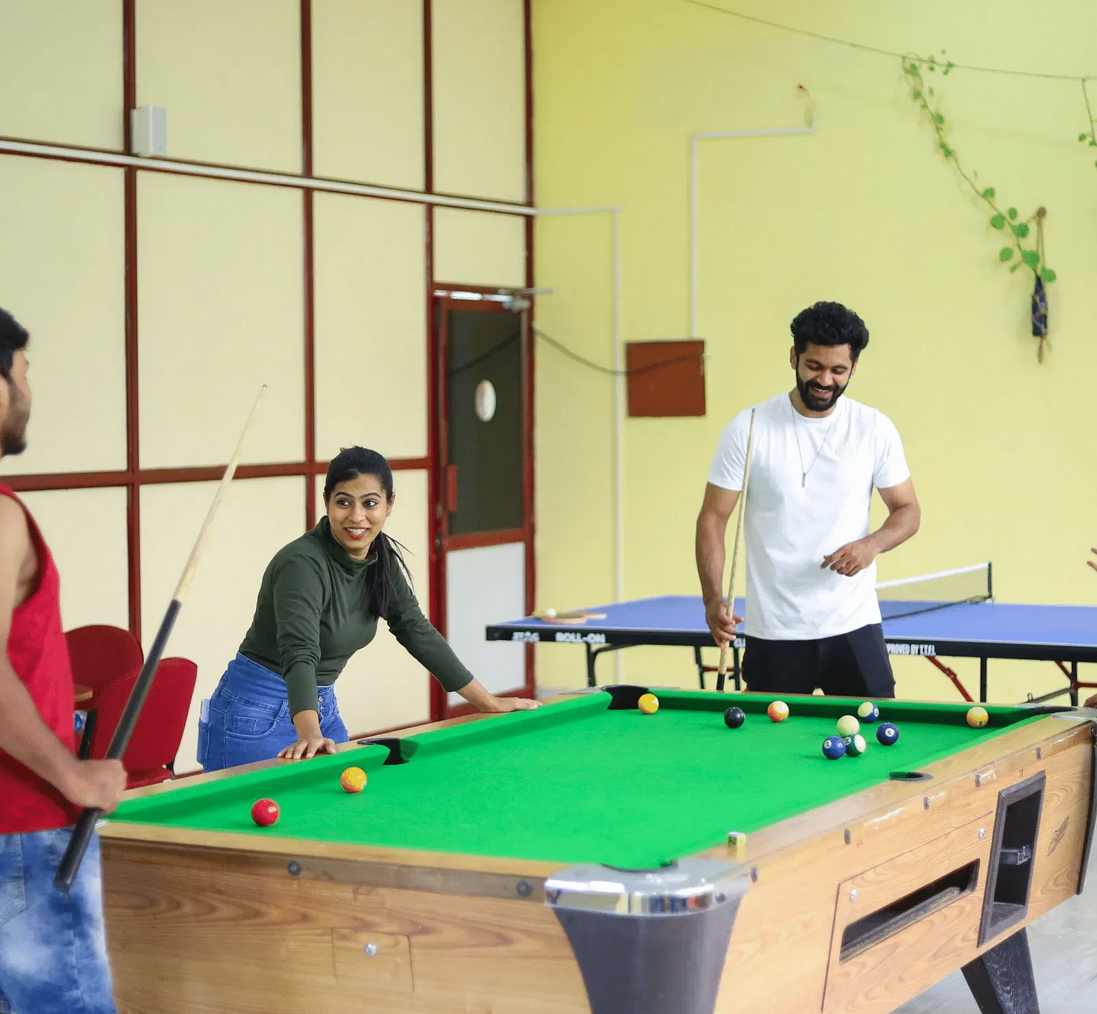 Three people playing pool in a brightly lit yellow room