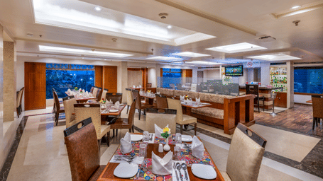 Blue Coriander Restaurant with four and six seaters and a bar counter with a wall mounted TV at Libra Lords Inn Jaipur