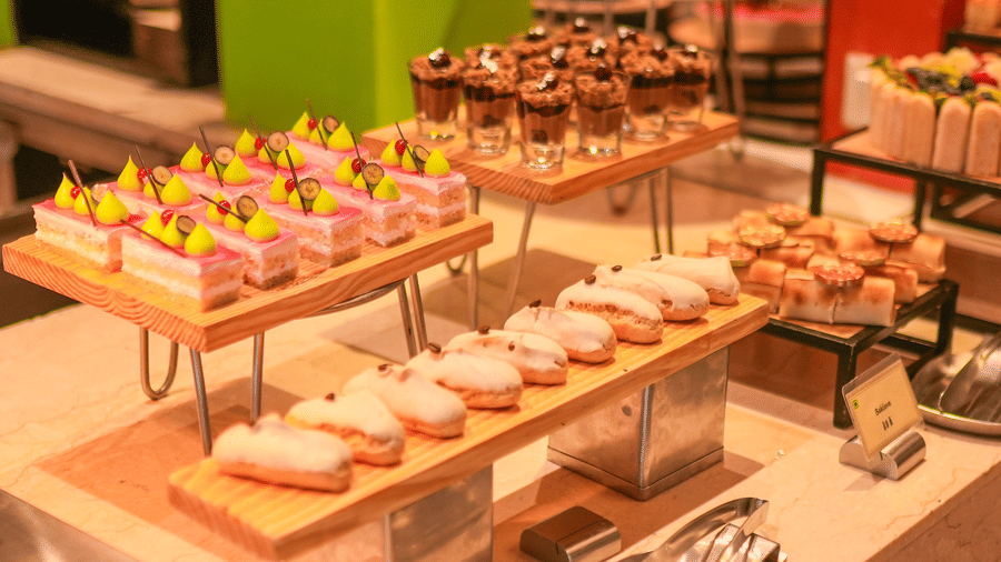 A dessert display with pastries arranged on tiered stands and rectangular trays at The Suryaa, New Delhi.