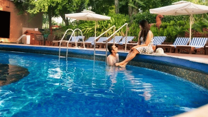 A view of the Swimming pool with a couple on the edge at Hotel Clarks Shiraz, Agra, one of the best Hotels with Spa in Agra