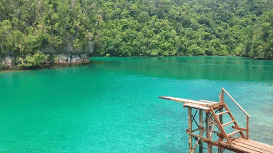 A wooden diving structure over the turquoise water of the Sugba Lagoon backed by lush green hills at Lamari Siargao.