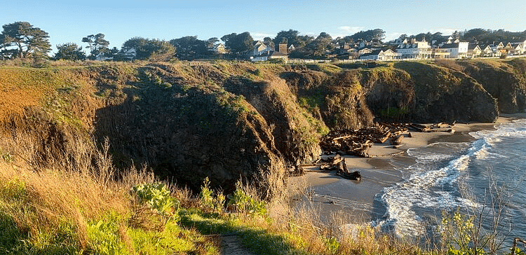 An image of a hill, below it there is a river, and beyond it there are houses surrounded by trees