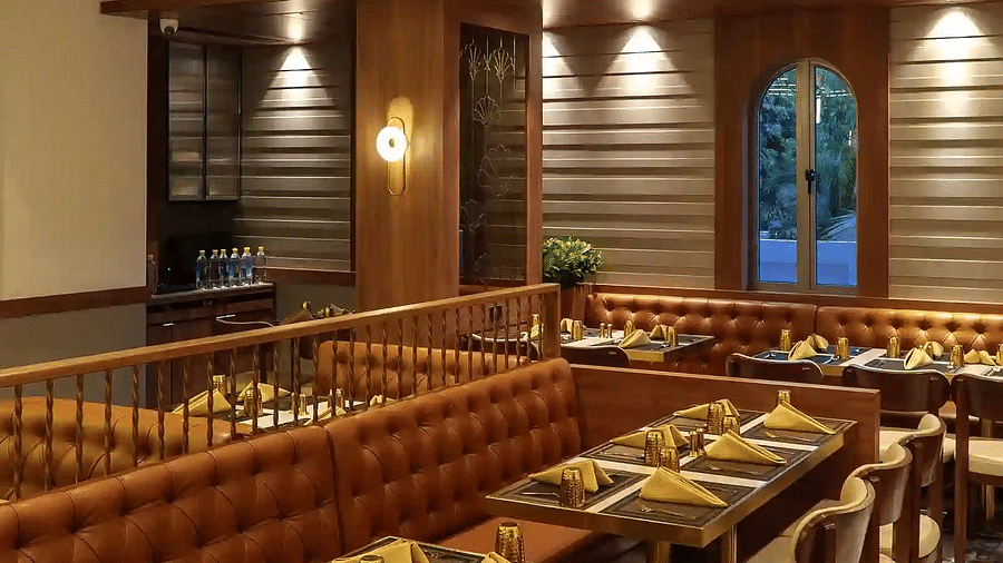 Neatly arranged seating tables with modern lighting and a double-door window and a CCTV at Naivedya Restaurant in Melior Inn, Mumbai.