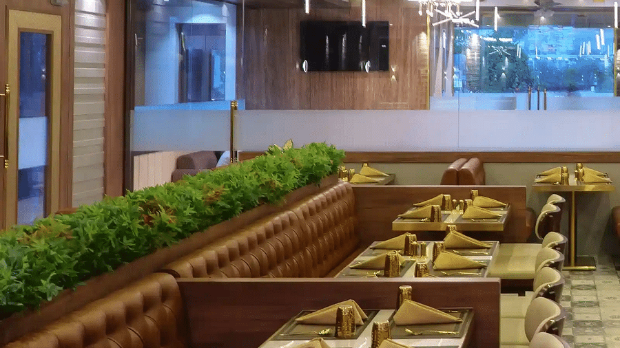 Straight view of dining tables with neatly placed cutlery arranged with glass doors and well-lit and decorated ceiling at Naivedya Restaurant in Melior Inn.