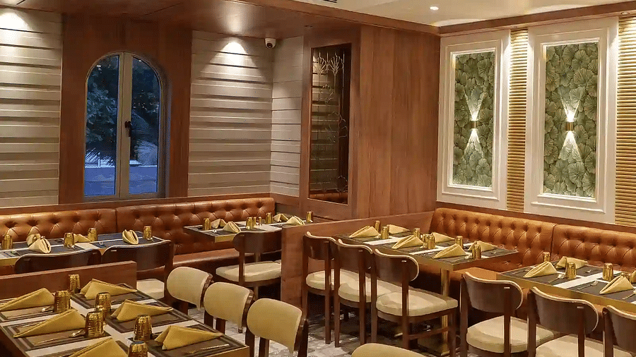 Neatly arranged seating tables with modern lighting and a double-door window and a CCTV at Naivedya Restaurant in Melior Inn, Mumbai.