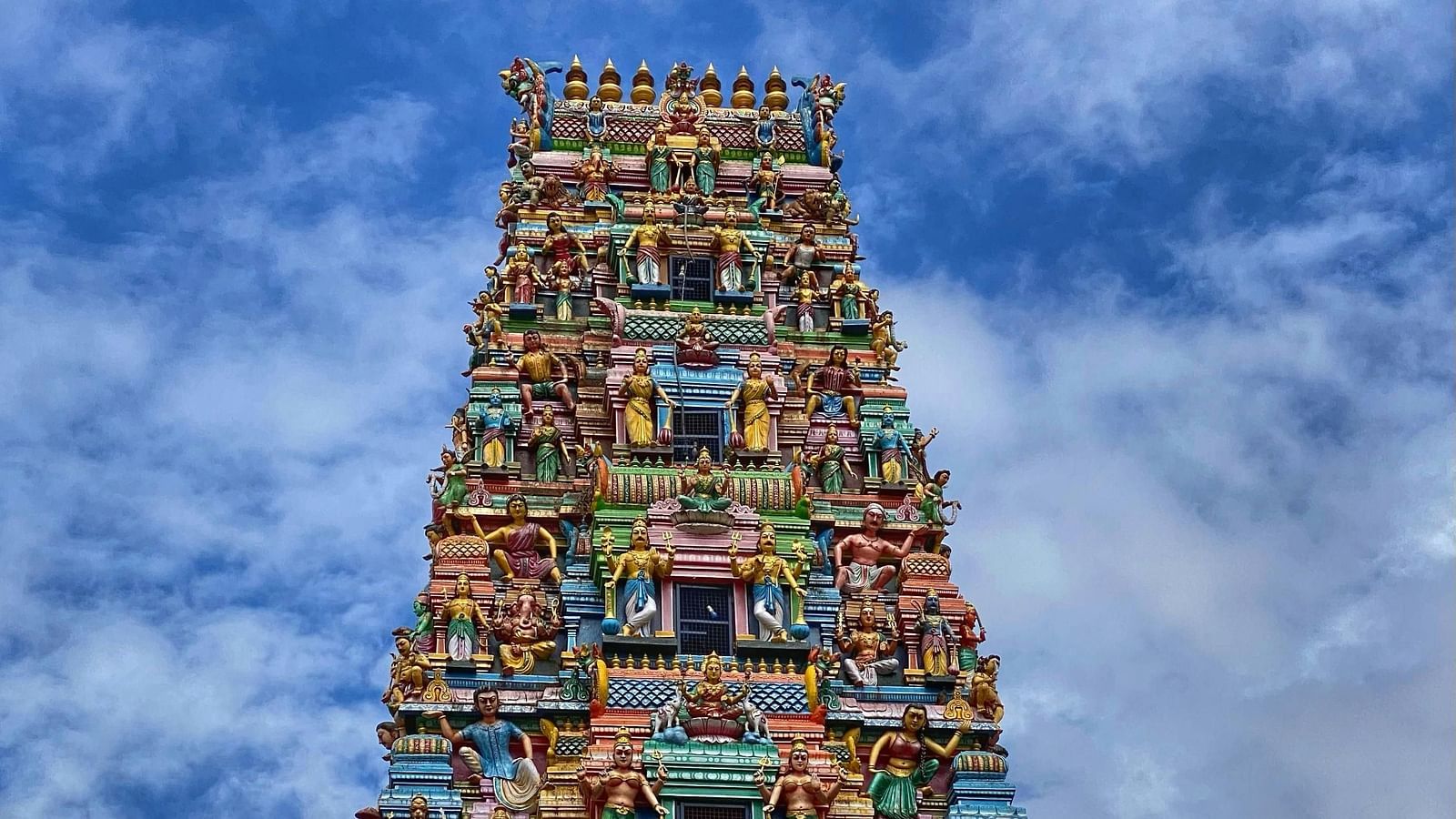 Colourful temple tower with intricate carvings against a clear blue sky.
