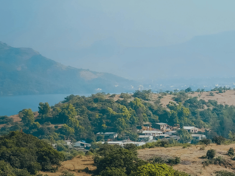 An aerial view of Lonavala with a lake and mountains in the distance, and buildings covered by trees in front of it. Adventure activities in Lonavala is hugely popular with numerous companies providing paragliding and much more.