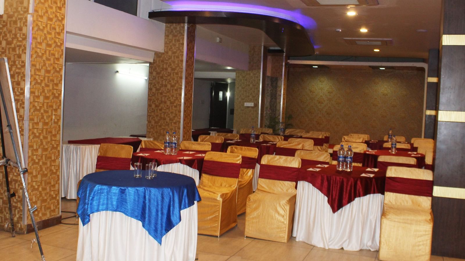 A banquet hall with round tables covered in blue and red cloths and amber-coloured chairs - TGI Apple Inn, Jaipur 