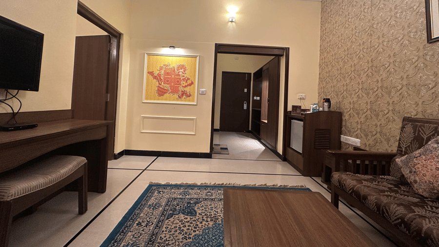 A living room entryway at Amantra Shilpi Resort, Udaipur features a wood desk, a small sofa, wall-mounted television, and a patterned rug on the floor.