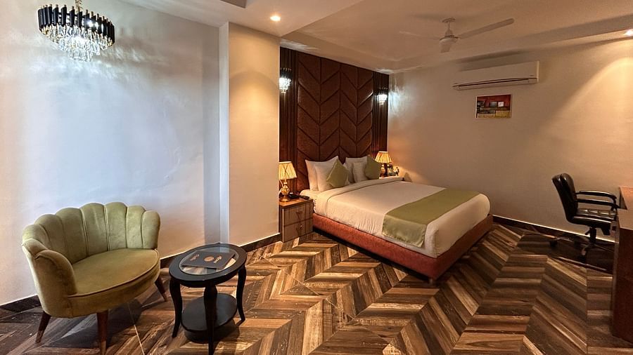 Image of Super Deluxe Room at DLS Grand Luxotica, Dehradun featuring a sitting space including a couch and a coffee table placed at a distance from the plush bed under warm lighting
