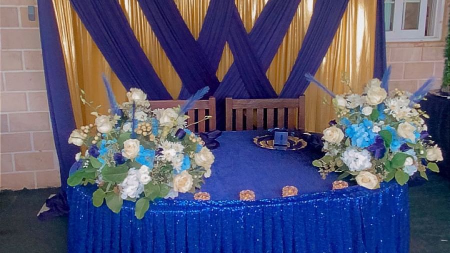 A round table with a tablecloth and floral arrangements against a navy blue and gold backdrop | A Stone's Throw Away