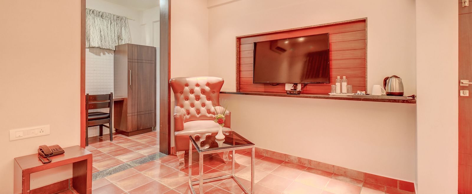 A room at Harigovinda's JNStay with a wall-mounted TV, a chair next to the doorway, and a bedside table