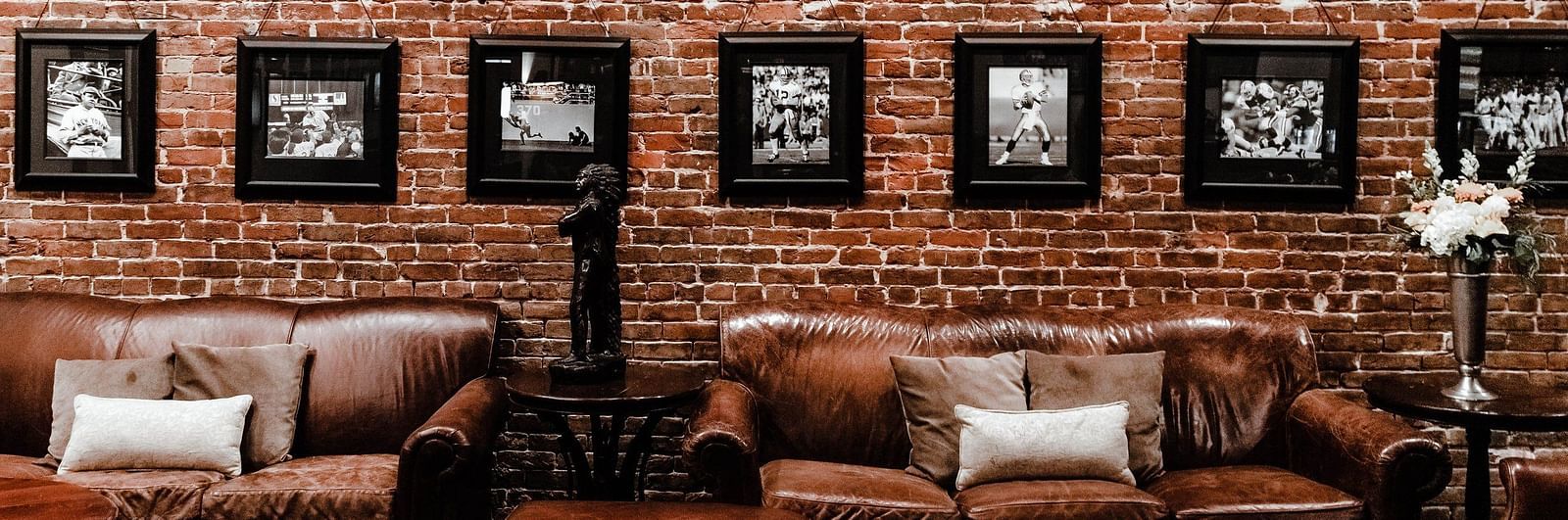 Sitting arena with brown sofas and wooden tables accompanied by brick textured wall with hanging wall art in the background 