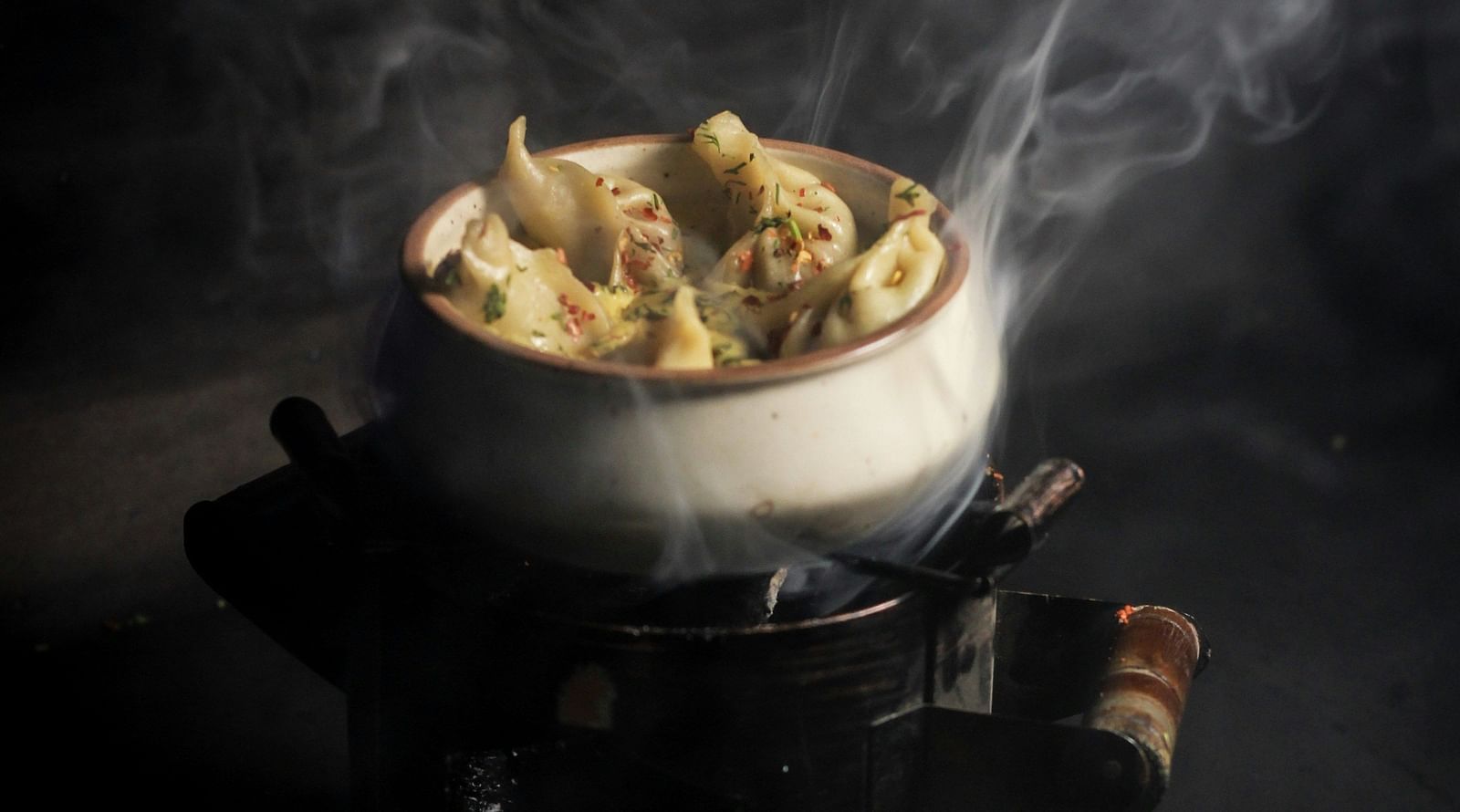 A plate of steaming hot momos with visible wisps of steam rising away.