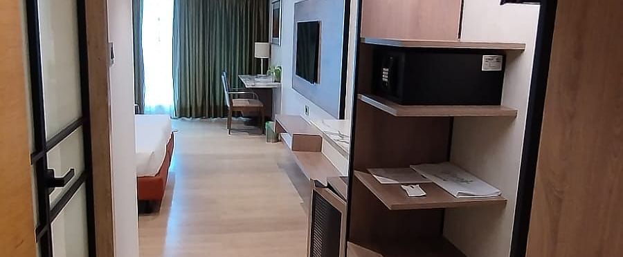 A view from the door way of an executive room in Mirage Hotel, featuring a wooden wardrobe area with a digital safe, and the entertainment unit.