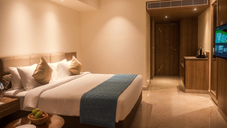 A Deluxe Room at Misty Ocean, Pondicherry, featuring a neatly made bed, a wall-mounted TV,  an A/C unit, and a bedside table.