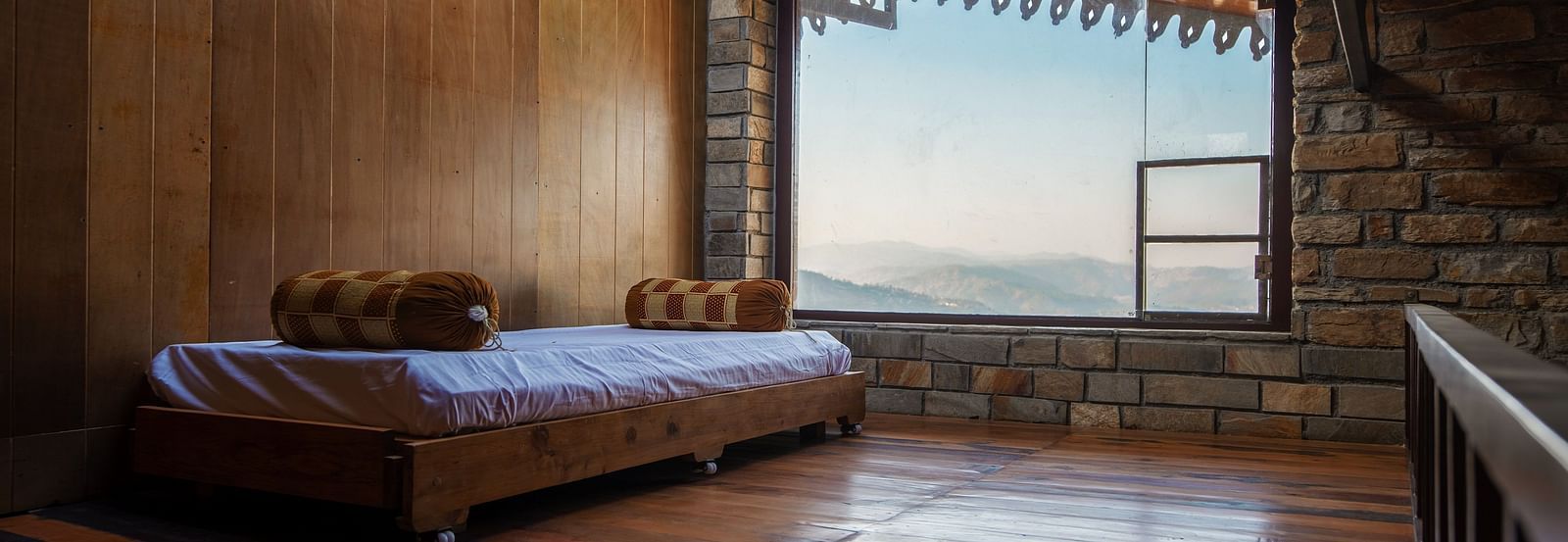 Rustic wooden bedroom interior with a bed and mountain view through a large window. - Blusalzz Homes The Himalayan Bungalow, Almora