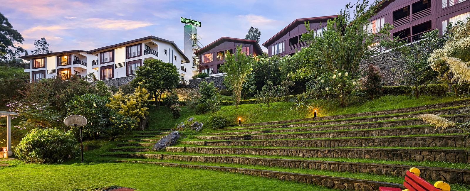 Exterior view of the hotel with lush greenery with the hotel buildings in the background - GReaT Trails Kodaikanal By GRT Hotels