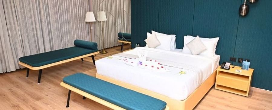 A bedroom in Dhanalakshmi Srinivasan Hotels, Perambalur, with a large bed, two lounge chairs, and two armchairs. The room features wooden flooring and a dark blue accent wall.