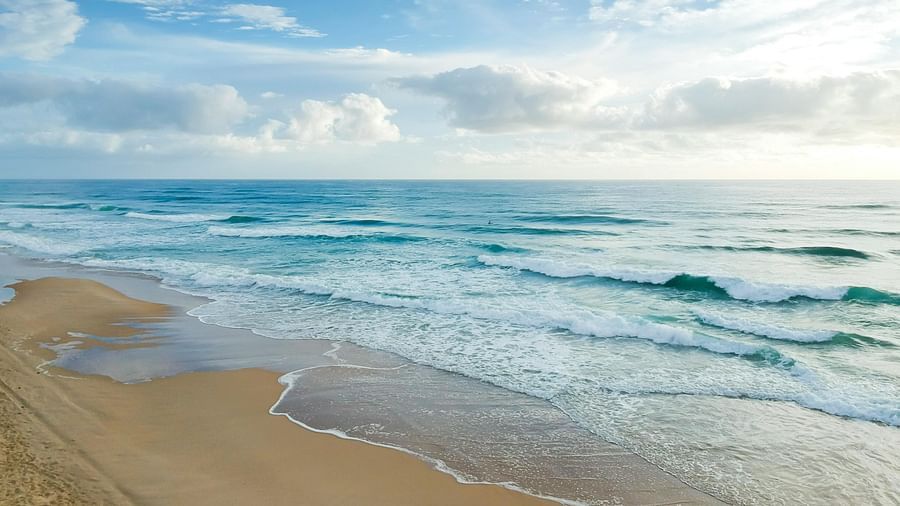 image of a clear beach side with blue sea waves crashing on the shoreline