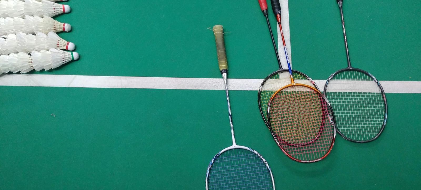 Top view of four badminton rackets and corks placed on a green court floor.