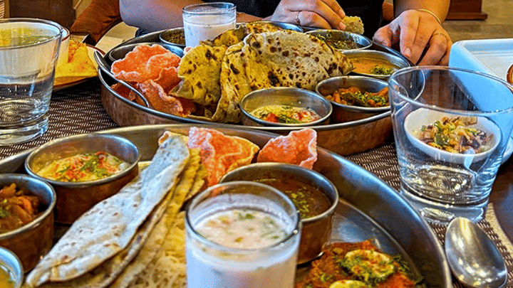 A woman sitting at a table at Rhythm Lonavala with multiple dishes placed in front of her as she smiles at the camera while preparing to eat the meal displayed on the table
