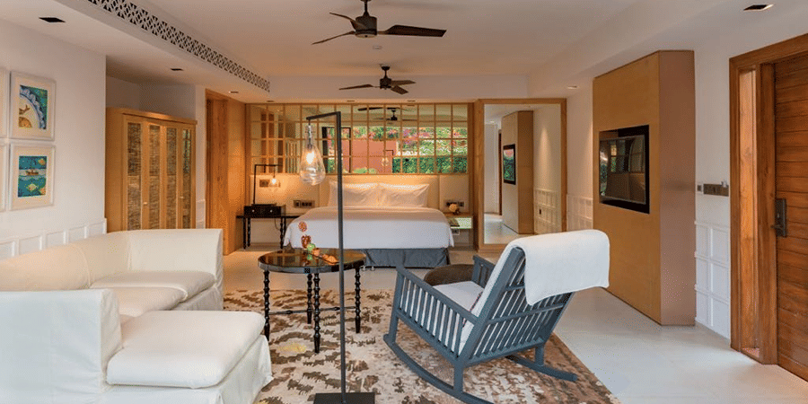 Villa room with a blue rocking chair and couches in front of a plush bed under warm lighting at Azaya Beach Resort in Goa with private pool