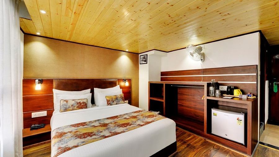 Image of a room with a bed and a wooden shelf on the side with a mini fridge in it at Yashshree Mall Road, Darjeeling.