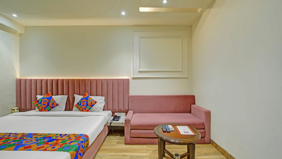Double bed with patterned runner, pink headboard wall, small seating area and wooden flooring at Hotel Maurya, Bhopal.