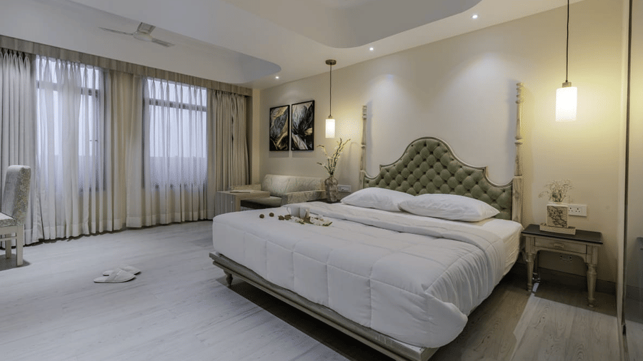 Full view of the Studio Room at Essentia Luxury Hotel and Convention, Nagpur, featuring a huge double bed with a tufted headboard along with thin linen curtains covering the windows.