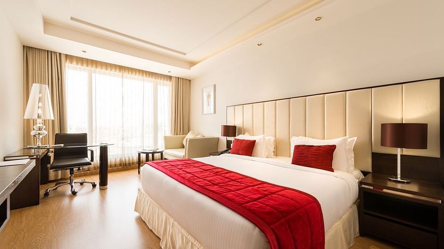 A well-lit hotel room with two twin beds covered in red bedspreads and white sheets - TGI Grand Fortuna, Hosur