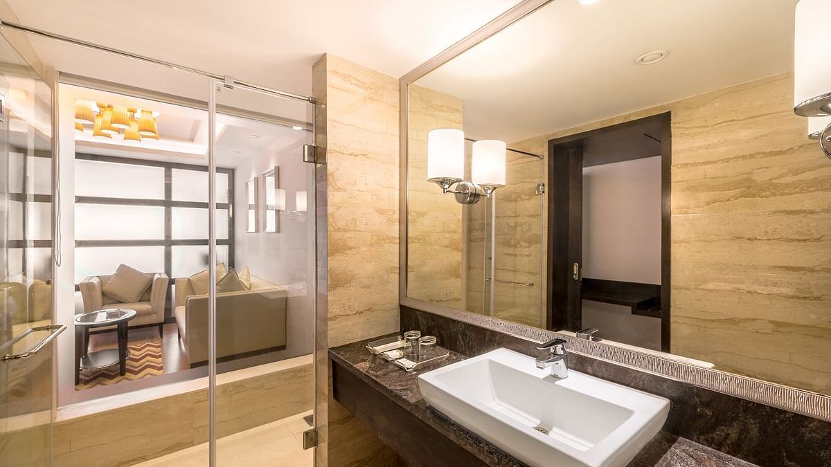 A bathroom with glass shower, large mirror and view into living area of the hotel room - TGI Grand Fortuna, Hosur