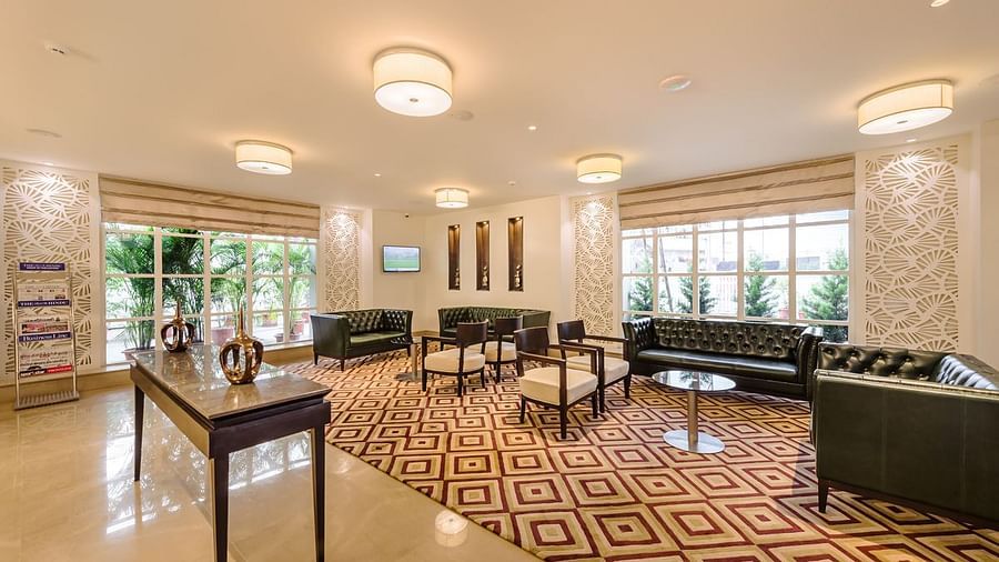 A brightly lit hotel lobby with a patterned rug, seating area and reception desk in the background - TGI Grand Fortuna, Hosur
