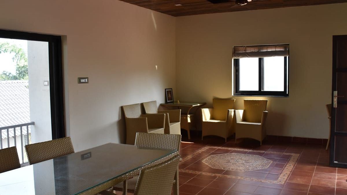 A dining area with a glass-topped table, tan chairs, a window, a dark ceiling fan, and a door leading outside.
